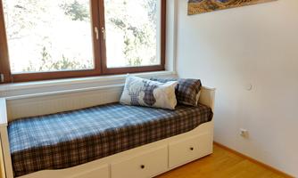 A cozy bedroom with a daybed and a modern wooden dresser. Large windows let in plenty of daylight and offer a view of the mountains.