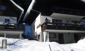 Two chalets in the snow with snow-covered roofs. In the background, snow-covered mountains can be seen.