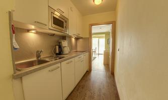 A modern kitchen with white cabinets and modern fixtures. The view leads into the adjoining room with a wooden floor.