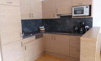 A modern kitchen with wooden furniture and a dark workspace. The appliances include a microwave and a coffee machine.