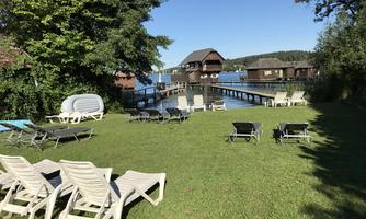 A beautiful garden by the water with loungers. In the background, wooden houses and a wooden bridge can be seen.