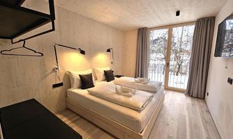 A modern bedroom with two single beds and a clean, minimalist design. Large windows offer a view of nature and provide plenty of daylight.