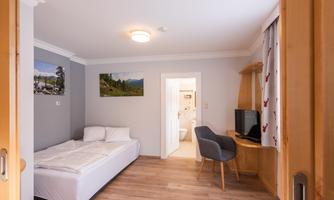 A simple room with a single bed and a desk. The walls are in soft colors and there are pictures of landscapes.