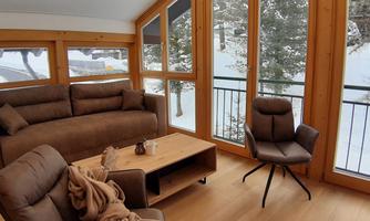 A cozy living space with brown furniture and large windows. Outside, snow and trees can be seen.