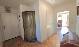 A bright hallway with wooden flooring. On the left side, there is an older wardrobe, and at the back, there is access to another room.