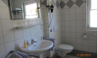 A modern bathroom with white tiles and a round sink. There are towels, a mirror, and a window with daylight.