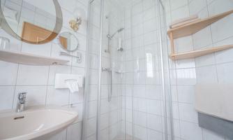 A modern bathroom with a shower cubicle and a sink. The walls are tiled and there are wooden shelves for towels.