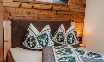 A cozy bedroom with wooden paneling and a large bed. The pillows have a traditional pattern, and above the bed hangs a picture of a picturesque landscape.
