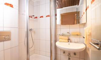 A modern bathroom with a shower and a sink. The white tiles and wooden ceiling create a bright and pleasant atmosphere.