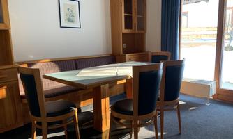 A cozy dining area with a wooden table and chairs. Lots of daylight flows through the windows, creating an inviting atmosphere.