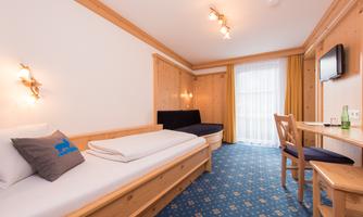 A cozy room with wooden paneling and a blue carpet. There is a single bed, a seating area, and a table with chairs.