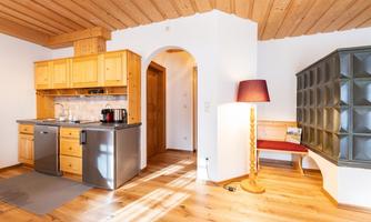 A modern kitchen with wooden cabinets and stainless steel appliances. The room has a warm wooden floor and a cozy seating area.