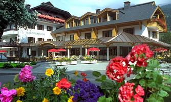 A charming hotel with an inviting outdoor area and colorful flowers in the foreground. It offers a cozy atmosphere with sun umbrellas on the terrace.