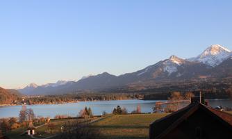 A picturesque landscape with a serene lake and snow-capped mountains in the background. The scene is illuminated by the setting sun in warm colors.