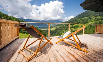 A cozy terrace with two loungers and a beautiful view of the green landscape. The sky is blue with some white clouds.