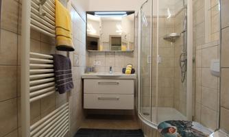 A modern bathroom with a shower and a bright tiled floor. Towels and toiletries are neatly arranged, and a large mirror reflects the space.