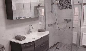 A modern bathroom with a glass shower and an elegant sink. The walls are light tiled, and there are soft towels on the shelf.