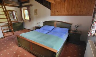 A cozy bedroom with a large bed and blue bed sheets. The room features wooden paneling and a window with curtains.