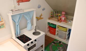 A children's room with a play kitchen and colorful storage boxes. A plush teddy bear and toys are also visible.