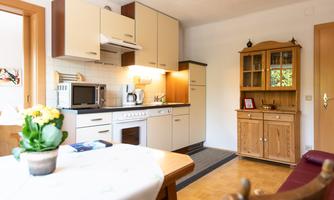 A modern kitchen with bright cabinets and a dining table. A vase of flowers is on the table and the room is well lit.