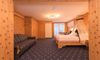 A cozy room with wooden paneling and a double bed. There is a seating area with a sofa and a desk.