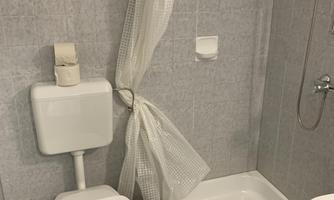 A bathroom with a toilet, a shower cubicle, and a sink. The walls are lightly tiled and there is a shower curtain.