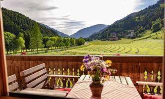 A beautiful mountain landscape with gentle hills and lush green. On the balcony, there are wooden chairs and a flower pot.