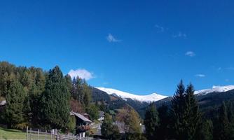 A picturesque landscape with a small village and a church. In the background, mountains stretch out with snow-capped peaks under a clear blue sky.