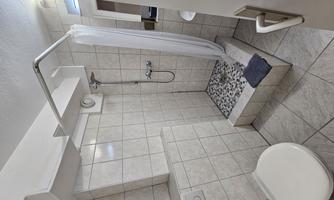 A simple, modern bathroom with a shower and toilet. The walls are covered with light tiles and there is a clear shower partition.