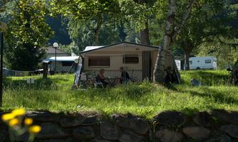 A cozy campsite with caravans and green areas. Two people are sitting outside relaxed and enjoying nature.