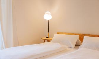 A quiet bedroom with two beds and white bedspreads. Next to the beds, there is an elegant lamp on a small table.