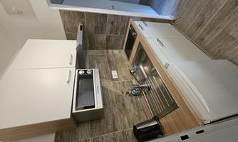 A modern kitchen with wooden details and white cabinets. It is compact and well-equipped with a refrigerator, sink, and microwave.