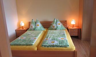 A cozy bedroom with a double bed and colorful bedspreads. The walls are light yellow, and two bedside lamps create a pleasant atmosphere.
