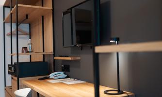 A modern workspace with a wooden desk, chair, and a television on the wall. Wooden shelves provide additional storage space.