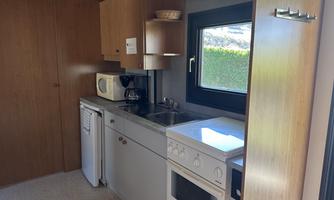 A modern kitchen with wooden cabinets and a large window front. It is equipped with a stove, microwave, and refrigerator.