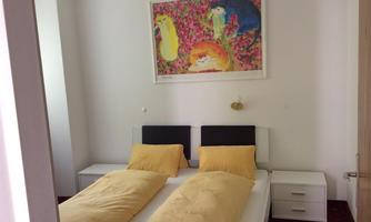 A cozy bedroom with two single beds and yellow bedspreads. A colorful painting hangs on the wall.