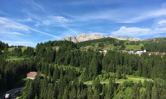 A picturesque mountain landscape with lush green forests and nearby mountains. In the foreground, a road runs through the beautiful nature.