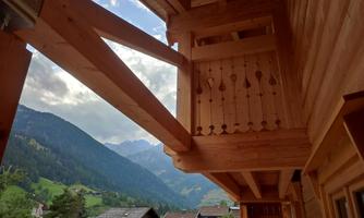 A wooden terrace with a view of the mountains. In the background, green hills and houses can be seen.