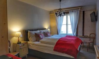 A cozy bedroom with a large bed and colorful cushions. The room has light curtains and modern lighting.