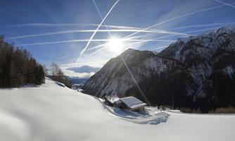 A winter landscape with snow and tall mountains. The sun shines over the scene and the sky is crisscrossed with contrails.