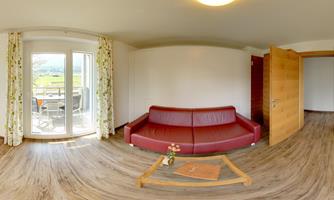 A cozy living room with a red sofa and a wooden table. Large windows offer a view of nature.