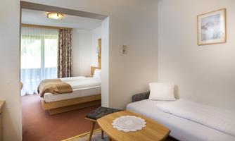 A cozy hotel room with a double bed and a single bed. The room is bright and features a small table as well as windows overlooking the outdoors.