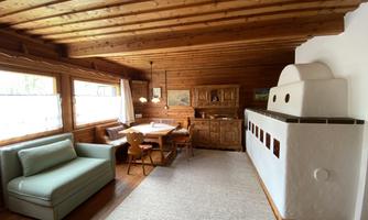 A cozy living space with wooden paneling and large windows. In the room, there is a sofa, a dining table, and a rustic wooden dresser.