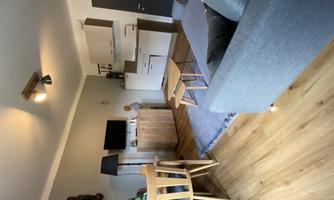 A modern living room with a cozy couch, a dining table, and a kitchen. The room is bright and inviting with wooden flooring and stylish furniture.