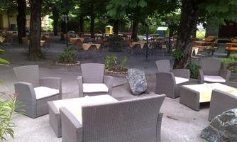 A cozy outdoor area with rattan furniture and green trees. Tables and chairs are set up for guests.