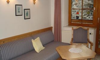 A cozy living space with a stripe sofa and a wooden chair. The winter landscape is visible through the window, and there are artistic wall paintings.
