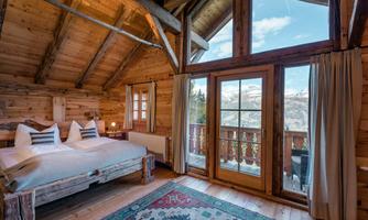 A cozy wooden cabin with a large bed and windows that offer a view of the mountains. The room has a warm and inviting ambiance.