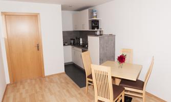 A modern kitchen with a small dining area. The table is decorated with a flower and the walls are bright and inviting.