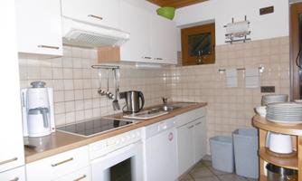 A modern kitchen with white cabinets and a tiled floor. There is a cooktop, an oven, and some kitchen appliances on the countertop.