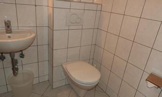 A simple bathroom with white tiles. It contains a sink, a toilet, and a small towel rack.